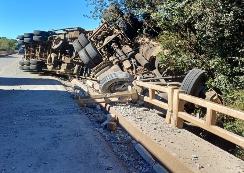Motorista fica soterrado por carga de cavacos após carreta capotar sobre ponte