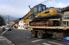 Caminhão transportando escavadeira enrosca em fiação e derruba poste