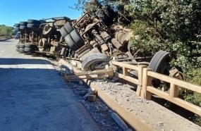 Motorista fica soterrado por carga de cavacos após carreta capotar sobre ponte
