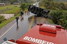 Carreta carregada com maçãs tomba, cai em açude e bloqueia rodovia